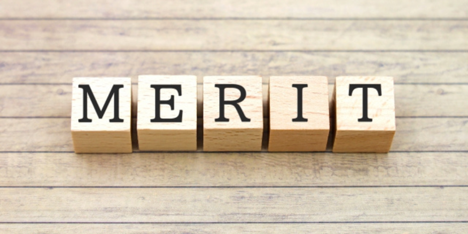 木のブロックに「MERIT」と書かれたシンプルな構成、木目の背景