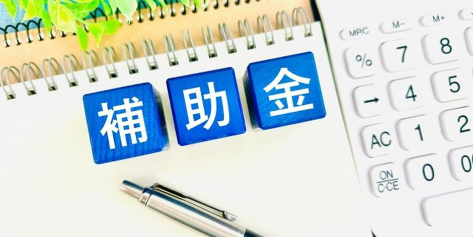 「補助金」の文字ブロックとノート、電卓、ペンが並ぶイメージ画像