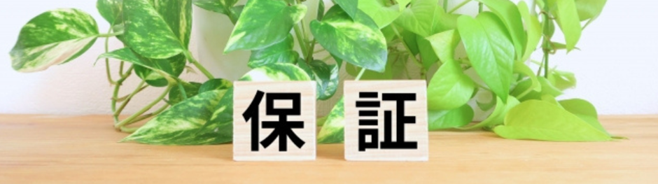 木製ブロックに「保証」と書かれ、背景に観葉植物がある画像